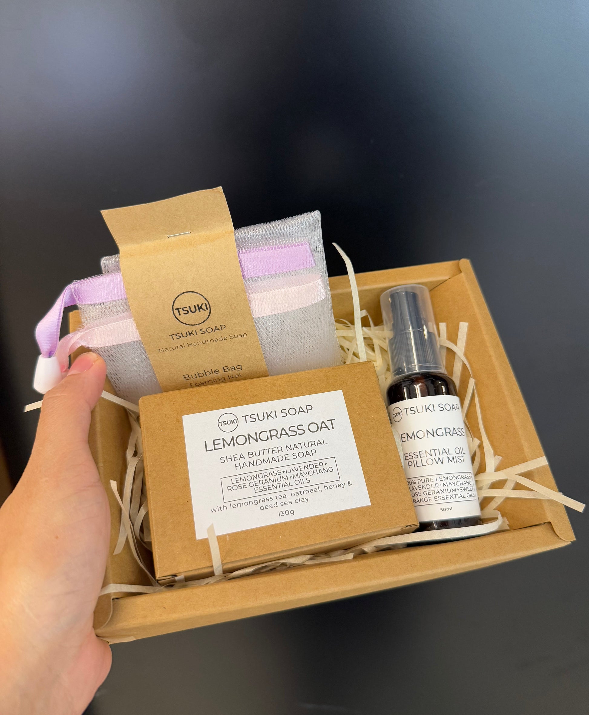 Hand holding a gift set with soap, towel, and bottle against a dark background